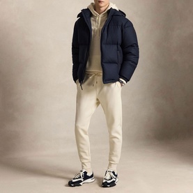 Model wearing Ralph Lauren Polo Player Double-Knit Joggers in Guide Cream with navy puffer jacket, cream hoodie, and black trainers.