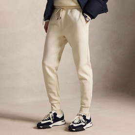 Model wearing Ralph Lauren Polo Player Double-Knit Joggers in Guide Cream with ribbed cuffs, styled with a navy jacket and chunky trainers.