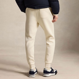 Model wearing Ralph Lauren Polo Player Double-Knit Joggers in Guide Cream with ribbed cuffs, styled with a navy jacket and navy trainers.