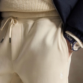 Model wearing Ralph Lauren Polo Player Double-Knit Joggers in Guide Cream with drawstring waist, styled with navy zip jacket and Polo watch.