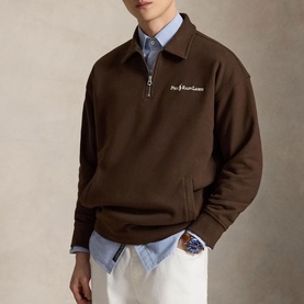 Model wearing Ralph Lauren Nutmeg Brown quarter-zip sweatshirt with embroidered logo, styled over a blue shirt with white trousers.