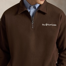Model wearing Ralph Lauren nutmeg brown half-zip sweatshirt with embroidered logo, styled over a light blue collared shirt.