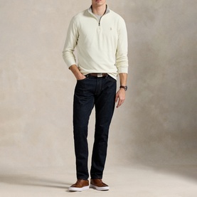 Model wearing Ralph Lauren cream quarter-zip sweatshirt with dark indigo jeans, brown belt, and canvas shoes.