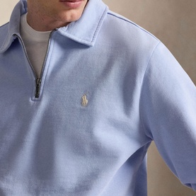 Model wearing Ralph Lauren Pebble Blue quarter-zip sweatshirt with embroidered Polo pony logo, styled over a white crew neck.