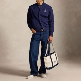 Model wearing Ralph Lauren Newport Navy sweatshirt with dark indigo jeans and white trainers, carrying a canvas tote bag.