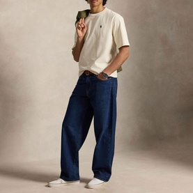 Model wearing Ralph Lauren cream T-shirt with small chest logo, styled with dark blue wide-leg jeans and white trainers.