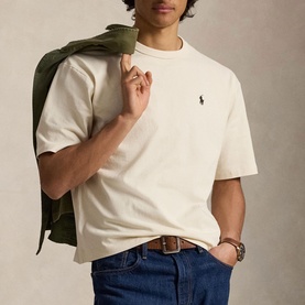 Model wearing Ralph Lauren Guided Cream T-shirt with embroidered pony logo, styled with blue jeans and olive jacket over shoulder.