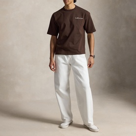 Model wearing Ralph Lauren nutmeg brown T-shirt with small chest logo, styled with white wide-leg trousers and white trainers.