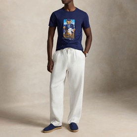 Model wearing Ralph Lauren Newport Navy Polo Bear graphic T-shirt, styled with white drawstring trousers and blue loafers.