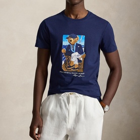 Model wearing Ralph Lauren Newport Navy Polo Bear graphic T-shirt, styled with white linen trousers and a watch.