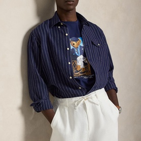 Model wearing Ralph Lauren Newport Navy Polo Bear graphic T-shirt, layered under navy pinstripe overshirt with white trousers.