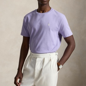 Model wearing Ralph Lauren Powder Purple crew-neck T-shirt with embroidered pony logo, styled with cream pleated trousers and a watch.