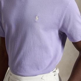 Model wearing Ralph Lauren powder purple T-shirt with embroidered polo pony logo, styled with white trousers.