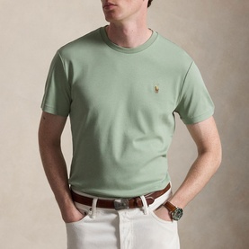 Model wearing sage green crew neck T-shirt with embroidered Polo pony, styled with white trousers and brown leather belt.
