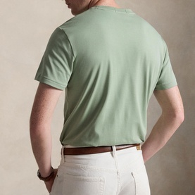 Model wearing a sage green crew neck T-shirt, styled with white trousers and a tan leather belt, seen from behind.