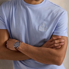 Model wearing Ralph Lauren Pebble Blue T-shirt with embroidered chest logo, arms crossed, styled with a silver watch.