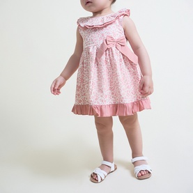 Model wearing Street Monkey Pink Print 2-piece baby set, floral dress with ruffle trim and bow detail, styled with white sandals