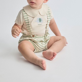 Model wearing Street Monkey Green/Ecru 2 Piece set; collared ecru tee with motif and green striped shorts with braces