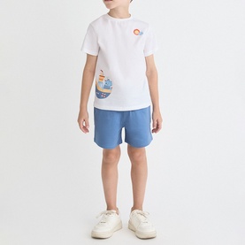 Model wearing Street Monkey White/Blue 2 Piece set, graphic tee with boat print and blue shorts, styled with white trainers