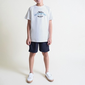 Model wearing Street Monkey White/Navy 2 Piece set; graphic T-shirt and navy shorts, styled with white trainers