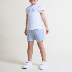 Child model wearing Street Monkey blue 2-piece set with white graphic tee and blue gingham shorts, paired with white trainers