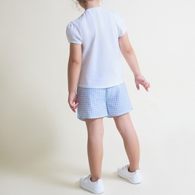 Model wearing Street Monkey blue 2-piece set with white short-sleeve top and blue gingham shorts, styled with white trainers.