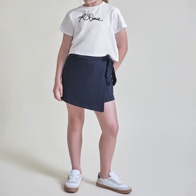 Model wearing Street Monkey White/Navy 2 Piece set, featuring logo tee and asymmetric wrap skort, styled with white trainers.