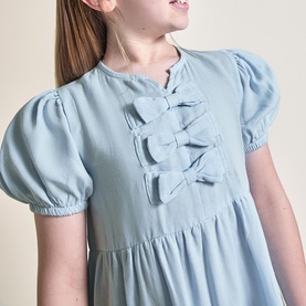 Model wearing Street Monkey blue dress with puff sleeves and triple bow detail on fitted bodice, empire waist silhouette