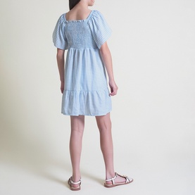 Model wearing Street Monkey blue gingham smocked dress with puff sleeves and tiered skirt, styled with pink sandals