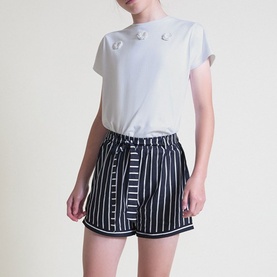 Model wearing Street Monkey white T-shirt with floral corsage detail, styled with navy striped shorts