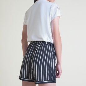 Model wearing Street Monkey white children's T-shirt, styled with navy and white striped shorts, seen from behind.
