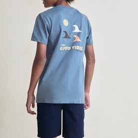 Model wearing Street Monkey blue t-shirt, back view showing surf fin graphic and "Only Good Vibes" slogan, styled with navy shorts.
