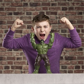 Boy posing with raised fists mimicking Superheroes Savage Smash Hulk green action figure on white surface, brick wall backdrop