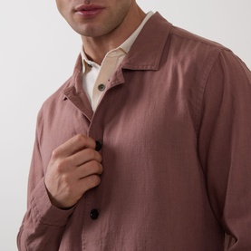 Model wearing Profuomo Garment-Dyed Overshirt in clay, linen-cotton blend with pointed collar and button fastenings, styled over cream polo shirt