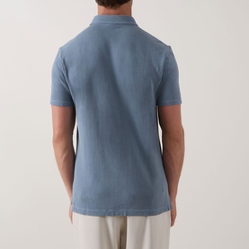 Model wearing Profuomo Garment-Dyed Polo Shirt in grey blue, rear view, showing polo collar and short sleeves, styled with light trousers.