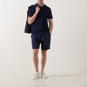 Model wearing Profuomo Solid Knitted T-Shirt in navy, styled with matching navy shorts and white trainers, holding a navy jacket over shoulder.