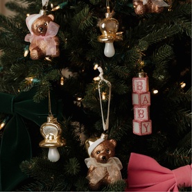 Pink and gold baby-themed Christmas tree ornaments including teddy bears, dummy, and letter blocks spelling BABY, styled on a decorated green tree
