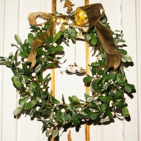 Vondels white tree decoration ornament displayed on a lush green mistletoe wreath with gold ribbon bow, hung on a white door.