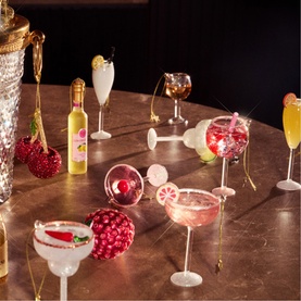 Collection of miniature cocktail glass and bottle Christmas tree ornaments arranged on a dark marble surface with warm lighting