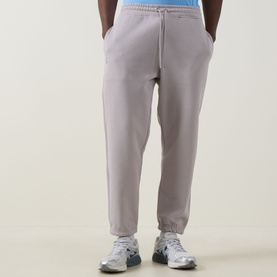 Model wearing On Running Club Collective Logo Sweat Pants in Ore, elasticated drawstring waist, cuffed hems, styled with white trainers.