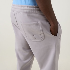 Model wearing On Running Club Collective Logo Sweat Pants in Ore, showing rear patch pocket with embroidered eyelet logo detail.