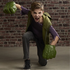 Child wearing Superheroes Hulk Gamma Smash Fists, oversized green foam fists on both hands, posed in action stance against brick wall background