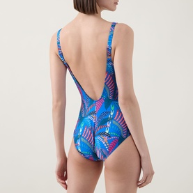 Model wearing Anita Elouise Floral Zip Swimsuit in Sardinia, showing low open back with shoulder straps and vibrant blue floral print.