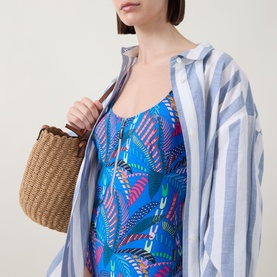 Model wearing Anita Elouise Floral Zip Swimsuit in Sardinia, styled with a blue striped shirt, carrying a woven basket bag.