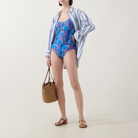 Model wearing Anita Elouise Floral Zip Swimsuit in Sardinia blue floral print, styled with striped shirt, woven bag and tan sandals.