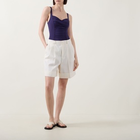 Model wearing Anita Michelle Ruched One-Piece Swimsuit in Blackberry, styled with white shorts and flat sandals.
