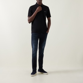 Model wearing Boss Black Casual black cotton polo shirt with dark wash slim jeans and white trainers.