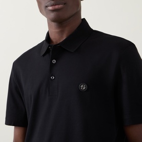 Model wearing Boss Black Casual black cotton polo shirt with tonal logo badge on chest and three-button placket.