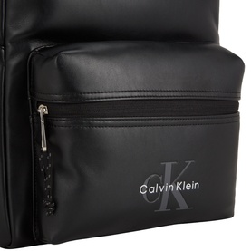 Calvin Klein black faux leather backpack, close-up of front zip pocket with embossed monogram logo detail and gold-tone zipper pull.