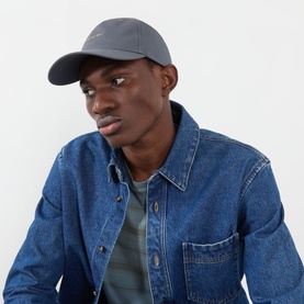 Model with Calvin Klein Logo UV Adjustable Cap in Turbulence grey, curved visor with logo lettering, worn with denim jacket